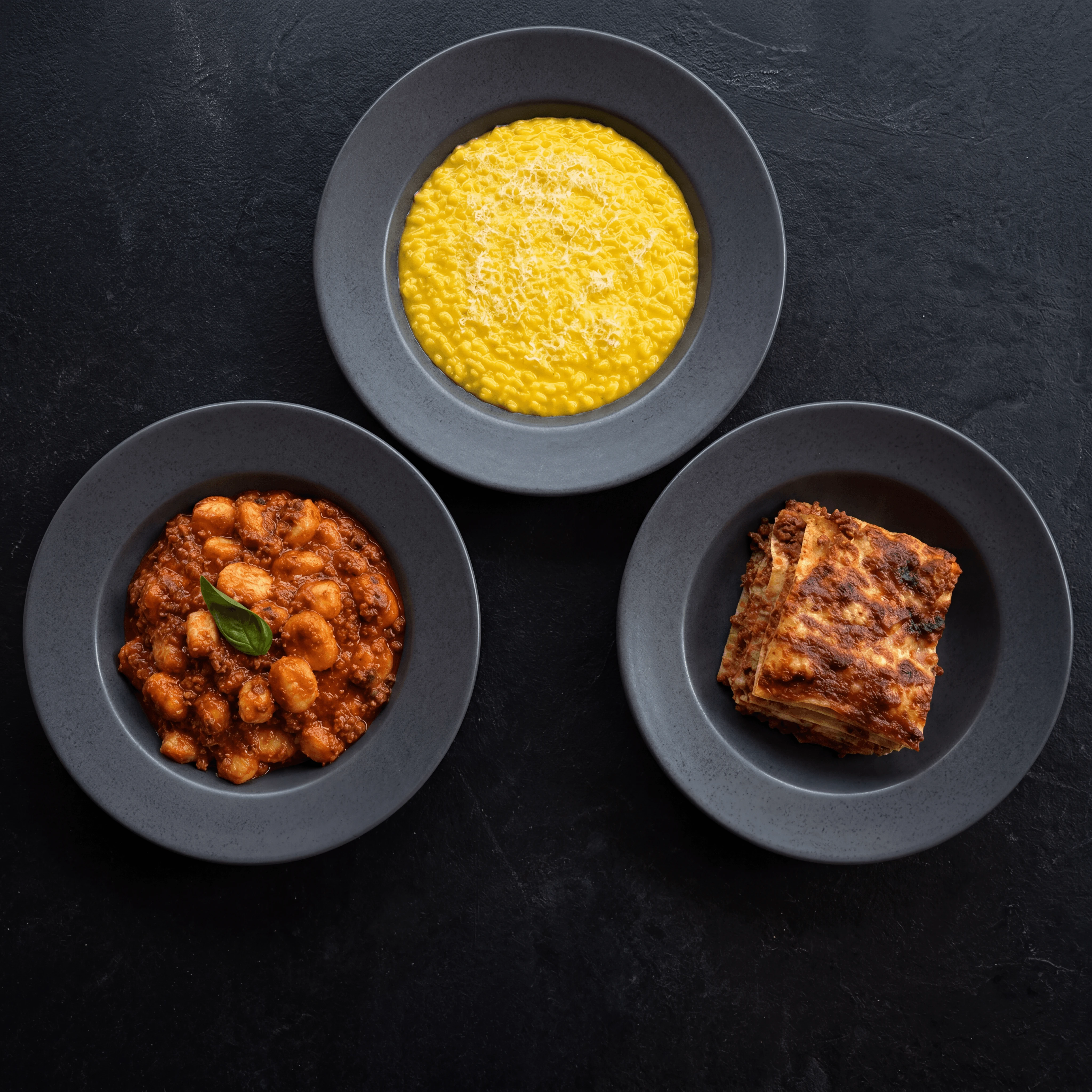 Italian primi trio risotto gnocchi lasagna overhead dark monolith — primi card photography