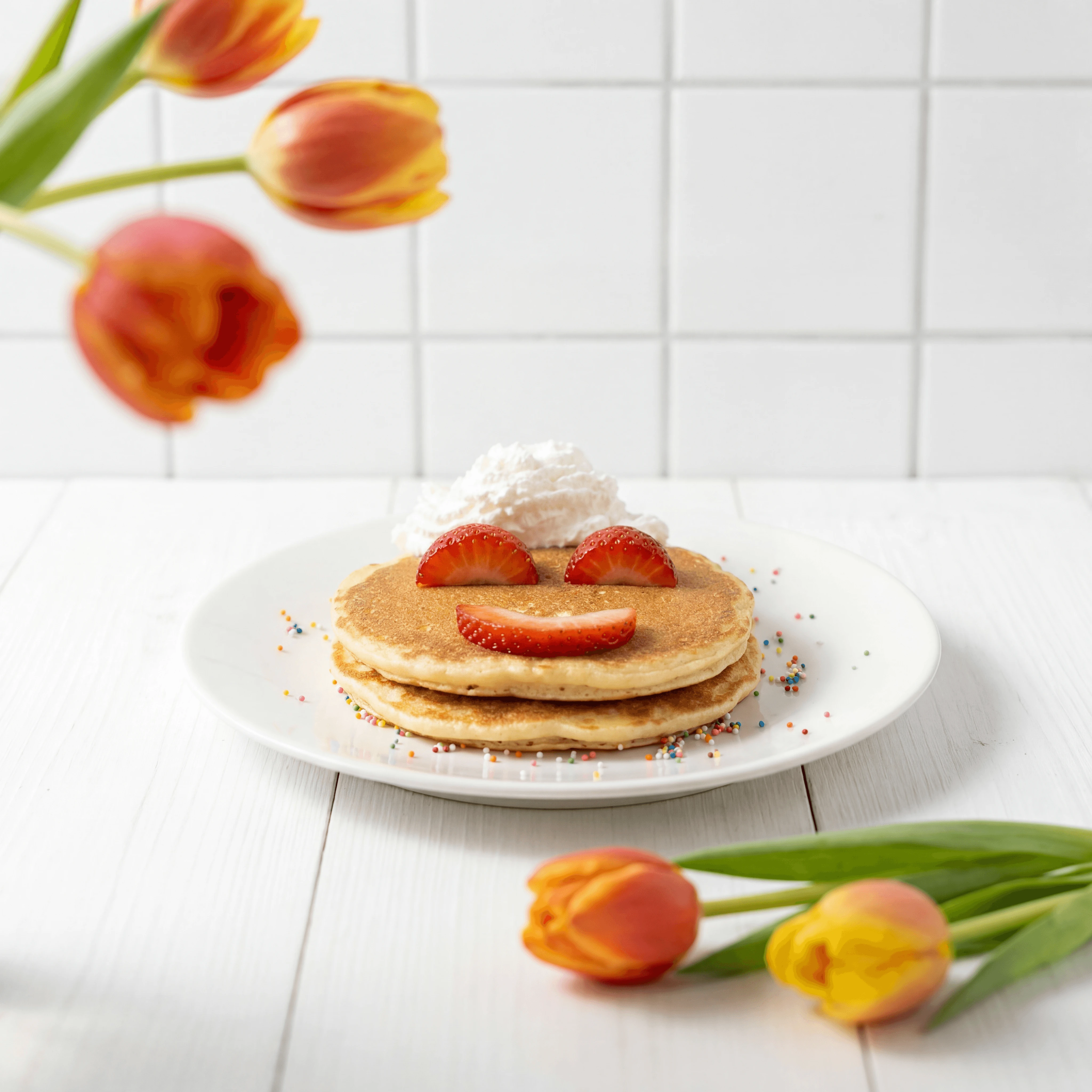 Smiling face short stack pancakes with strawberry eyes whipped cream cloud — kids brunch menu photography