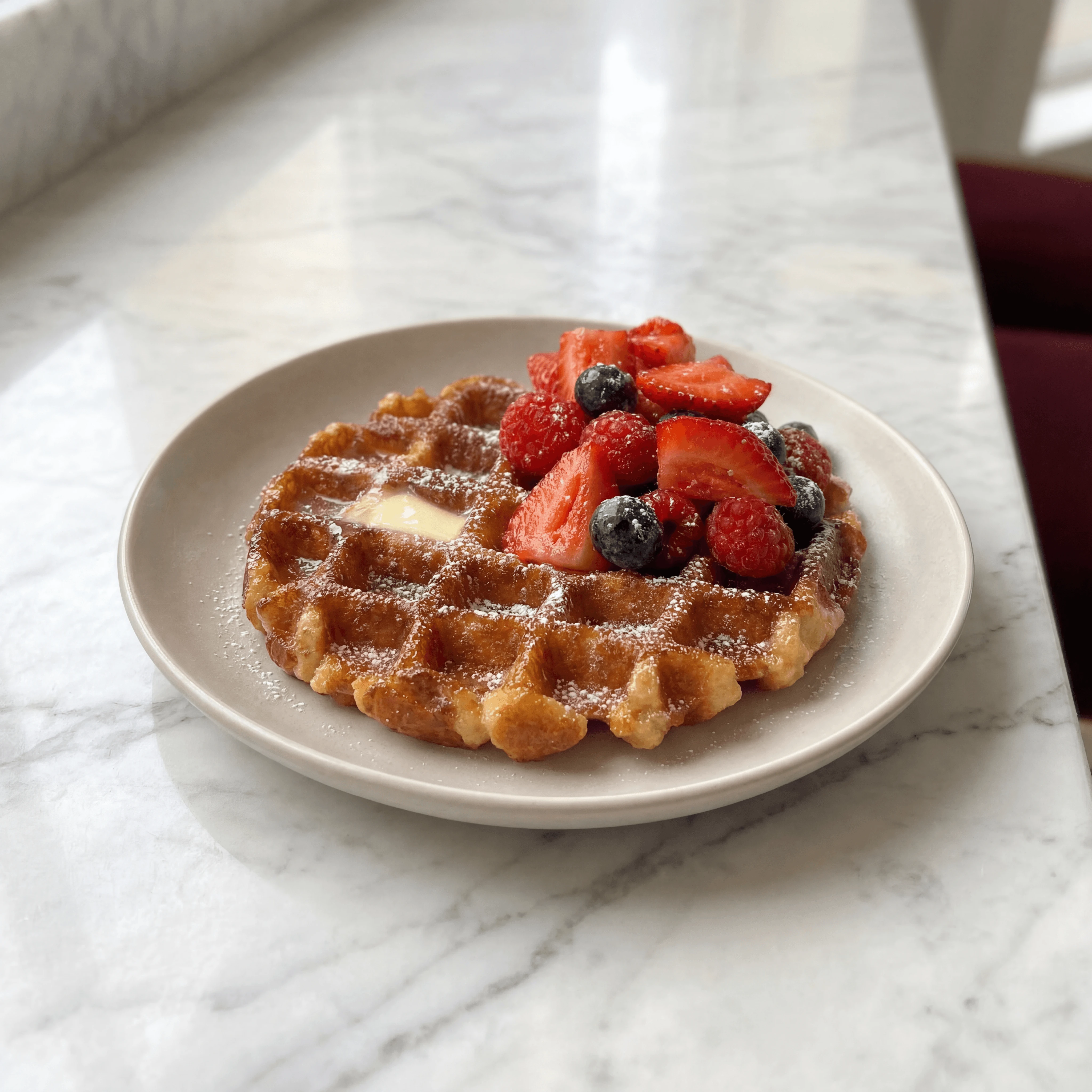 Belgian Liege waffle with melting butter pat and fresh strawberry blueberry crown — brunch menu photography