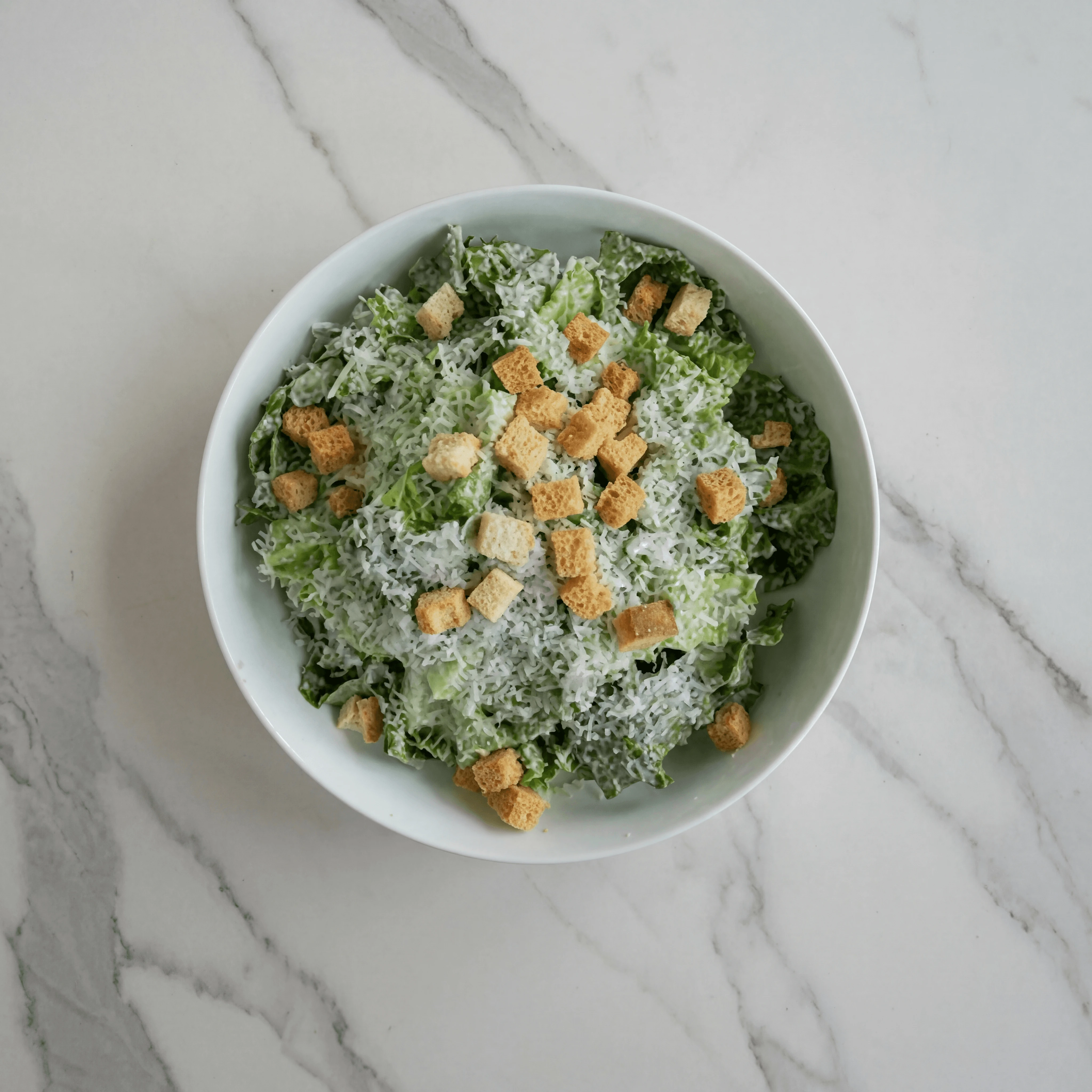 Single Caesar salad romaine parmesan croutons marble overhead — iconic salad FAQ sidebar photography